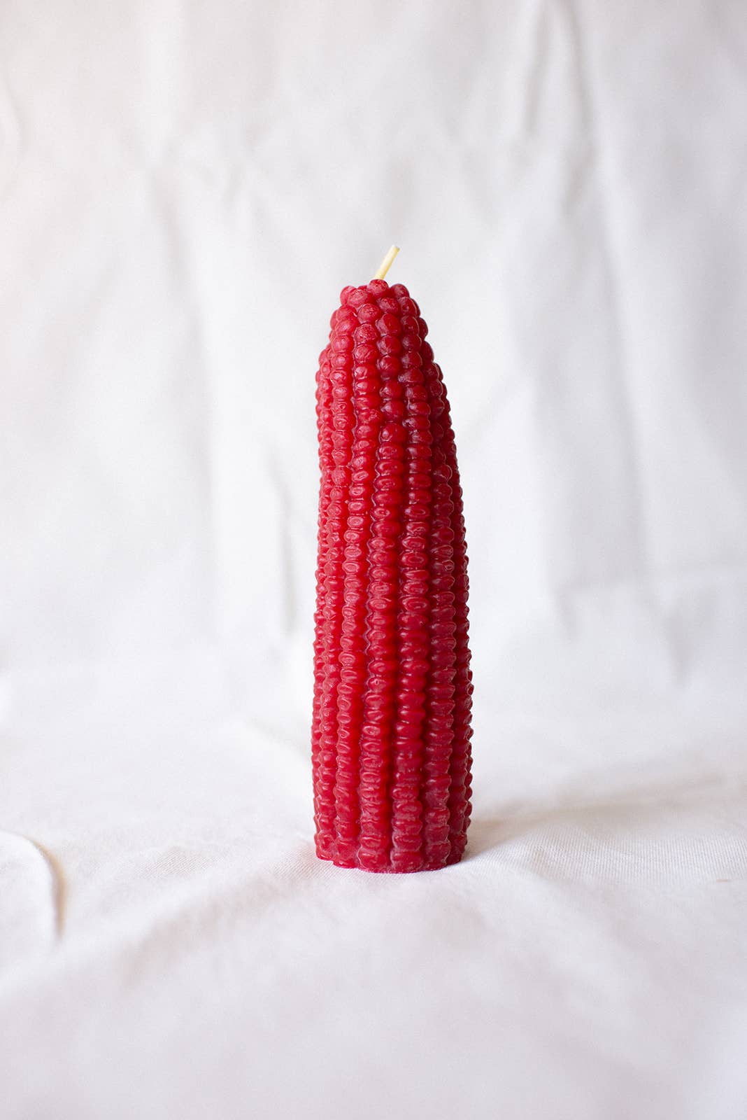 Two corn-shaped candles, one yellow and one red, on a white fabric background.
