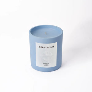 A blue candle with a label that reads 'berrybomb amoln' and has a branding symbol on it.