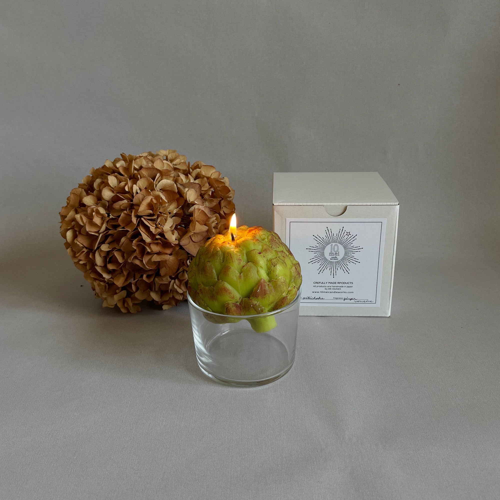 An artichoke candle with a glass, dried flowers, and a white box. 