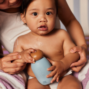 A woman holding a baby and a bottle of Nemah baby lotion. 