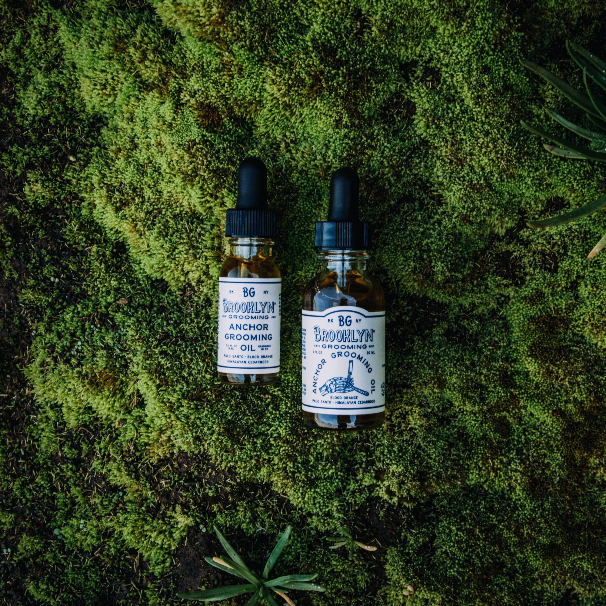 Two bottles of anchor grooming oil on a mossy background. 