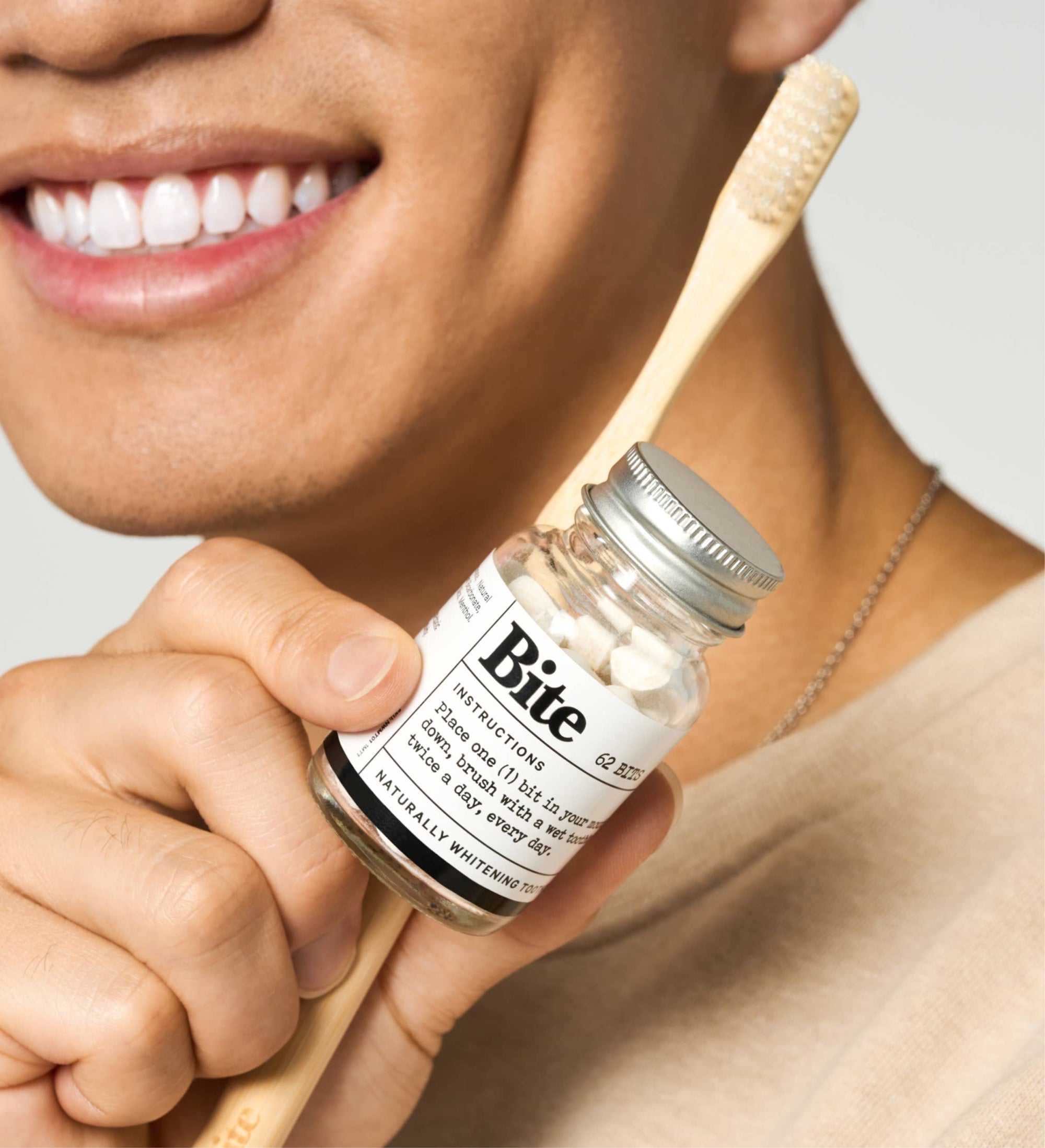 A glass bottle labeled 'bite' containing toothpaste bits, with a few toothpaste bits scattered outside the bottle on a white background.