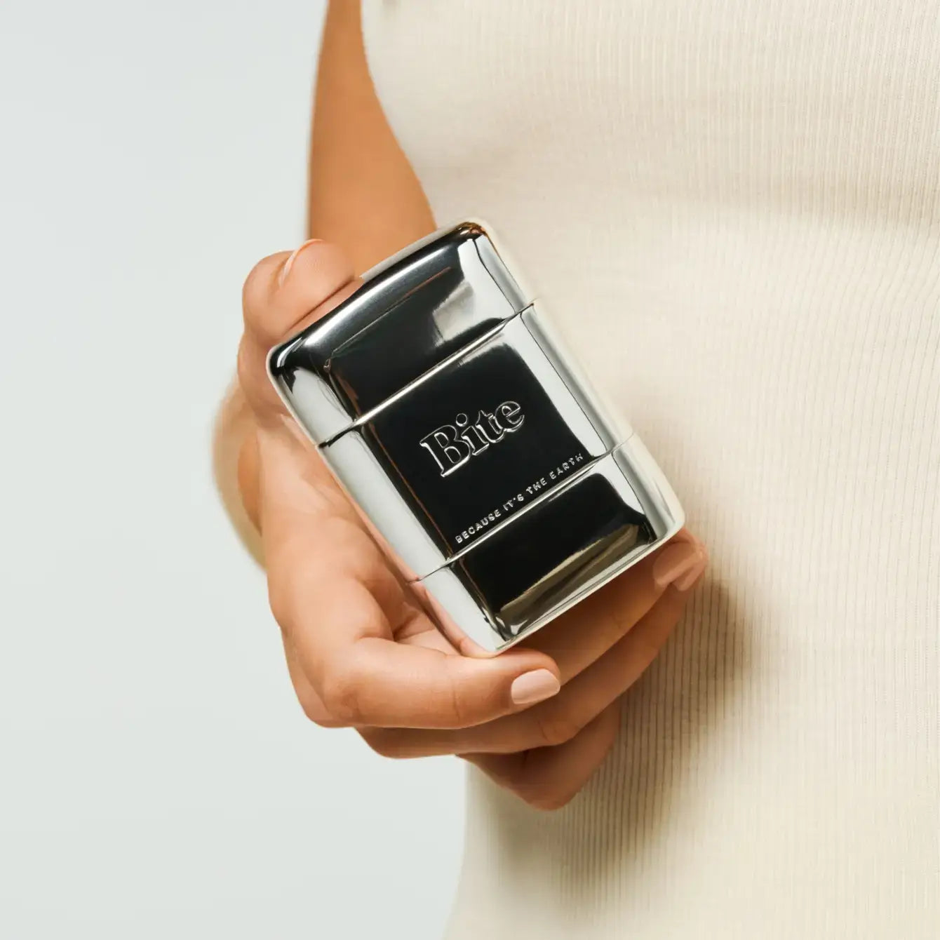 A hand holding a silver aluminum deodorant case with a clasp closure, branded with the word 'bite' on the front.