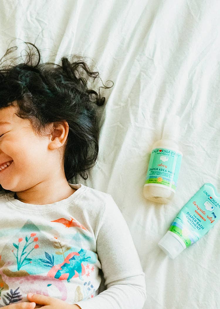 Child lying on a white blanket with two bottles of natural baby products.