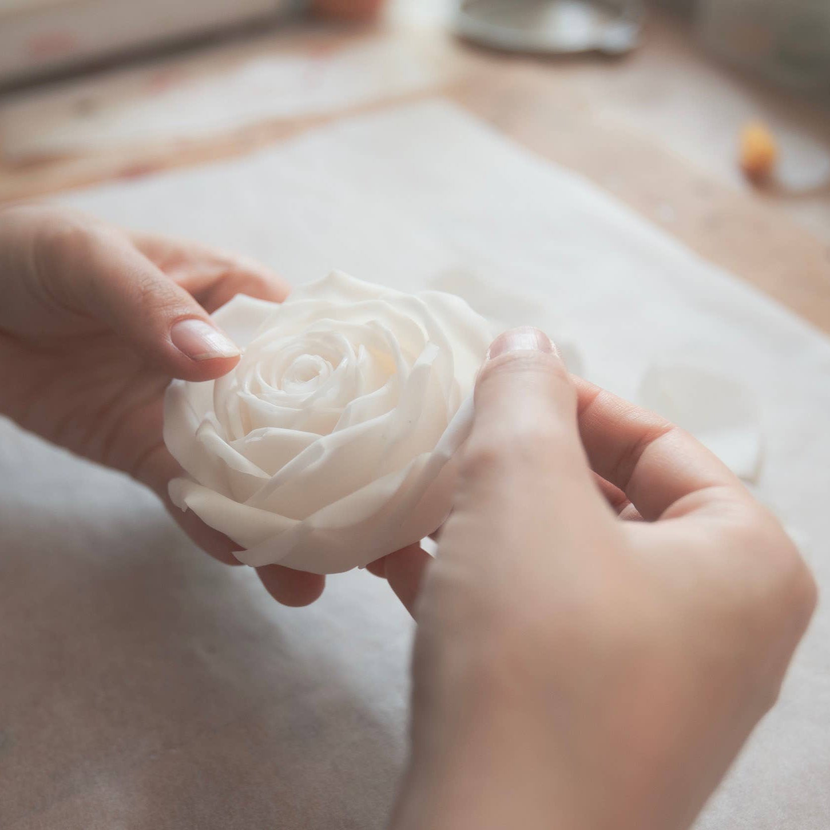 A person assembling a candle shaped like a rose. 