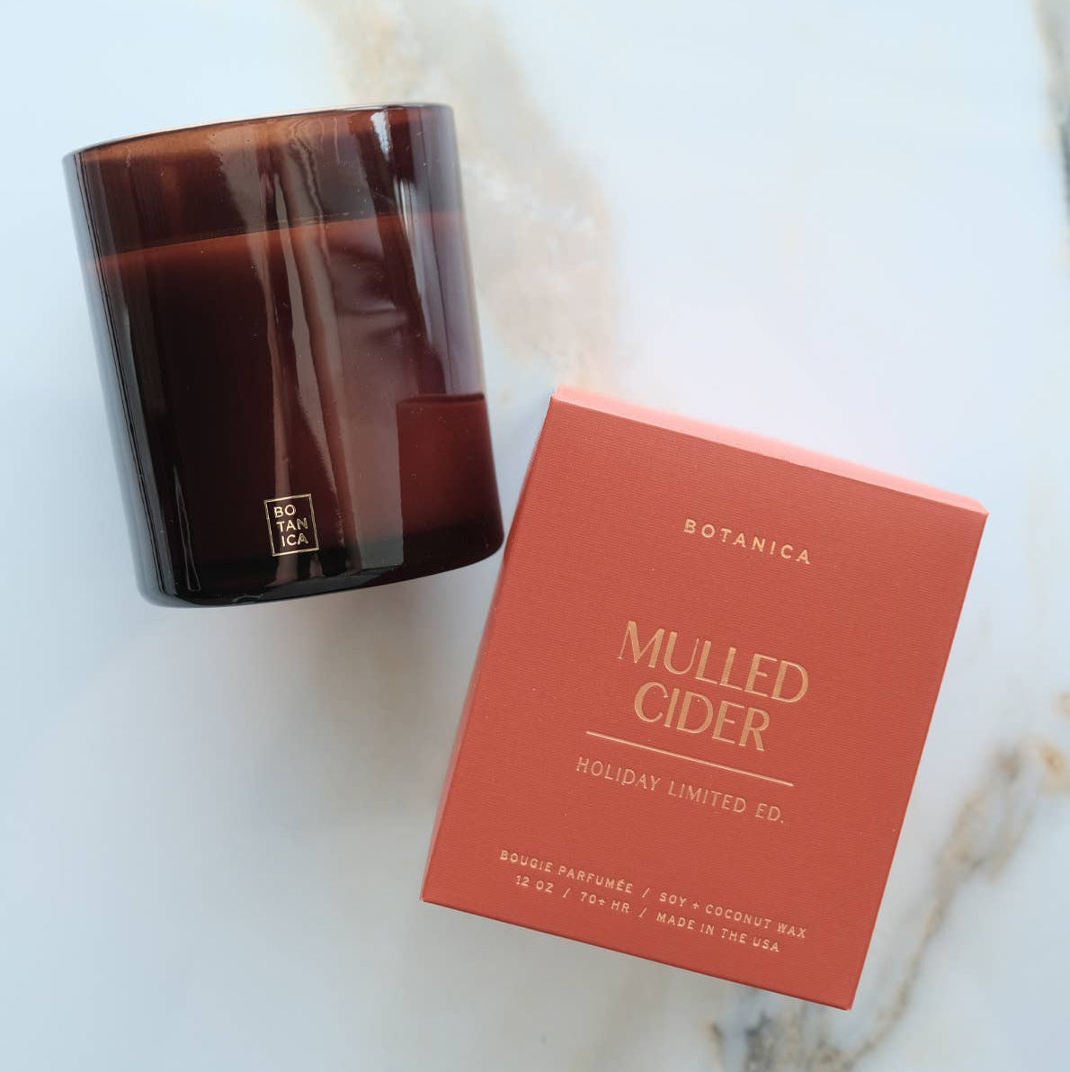 Candle with a lit wick and its packaging on a gray background
