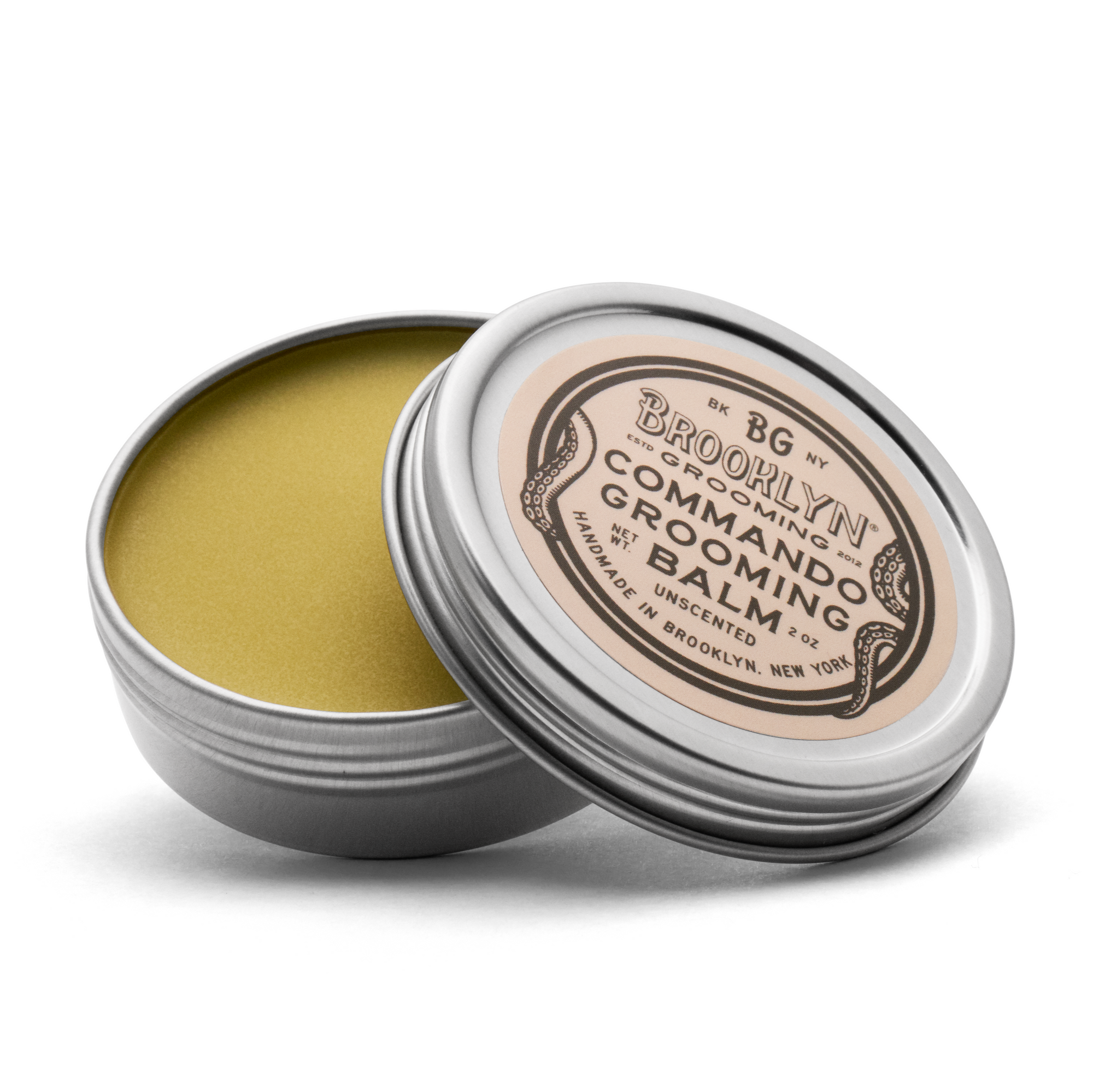 A metal tin with a removable lid containing a yellowish solid grooming balm. The label reads 'Brooklyn Grooming Commando Grooming Balm'.