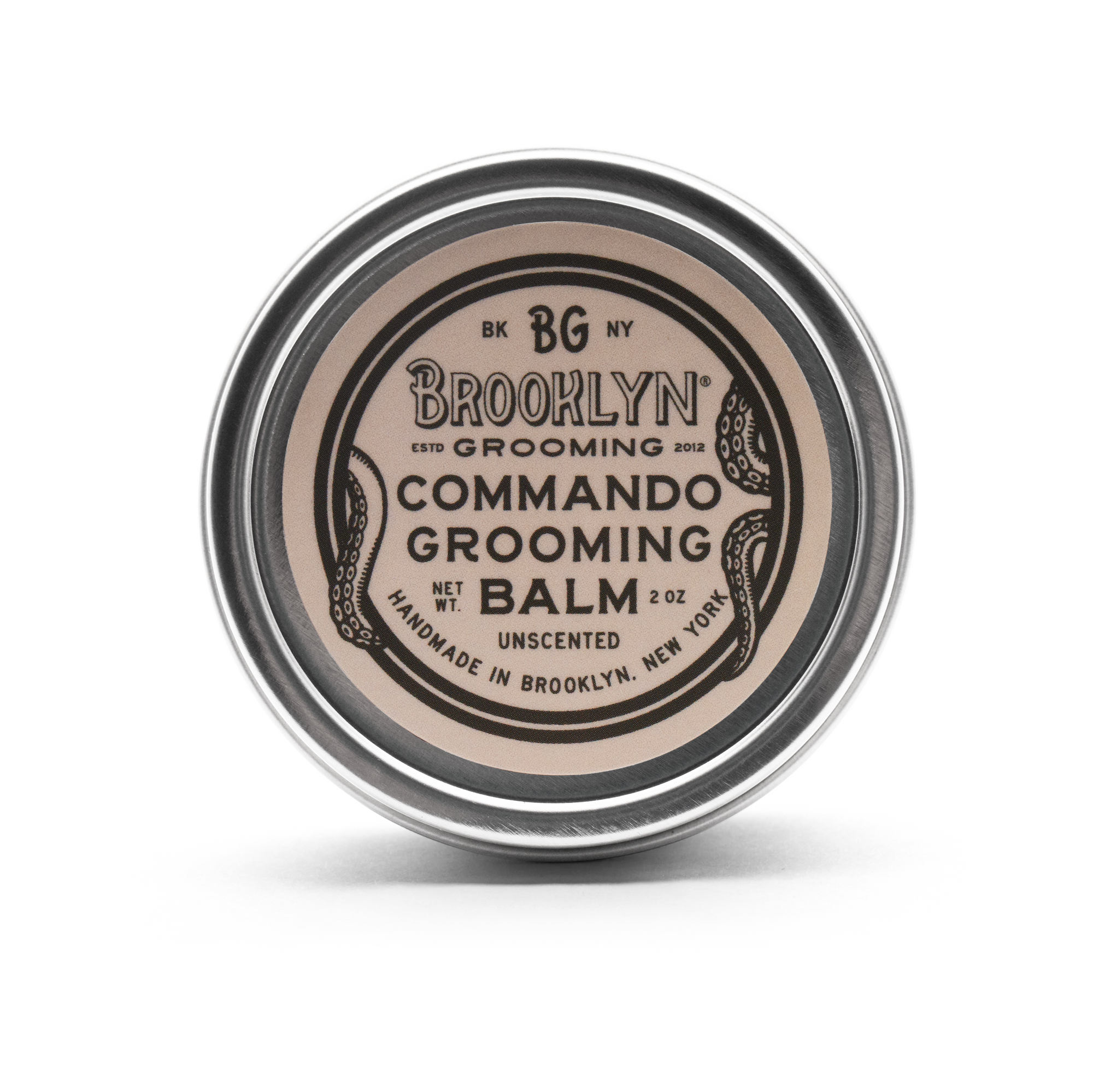 A metal tin with a removable lid containing a yellowish solid grooming balm. The label reads 'Brooklyn Grooming Commando Grooming Balm'.