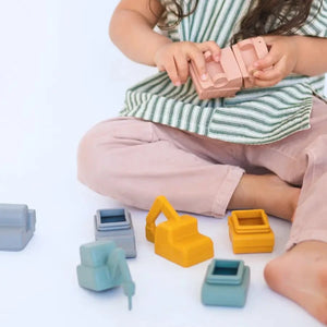 A child wearing light pink pants and a striped shirt playing with the Bug + Bean Construction Mold - Free Bath Set.