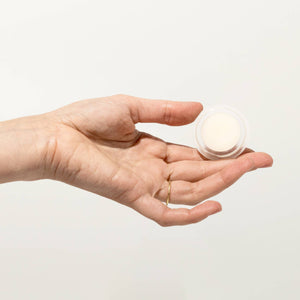 Hand holding a small white container against a light background
