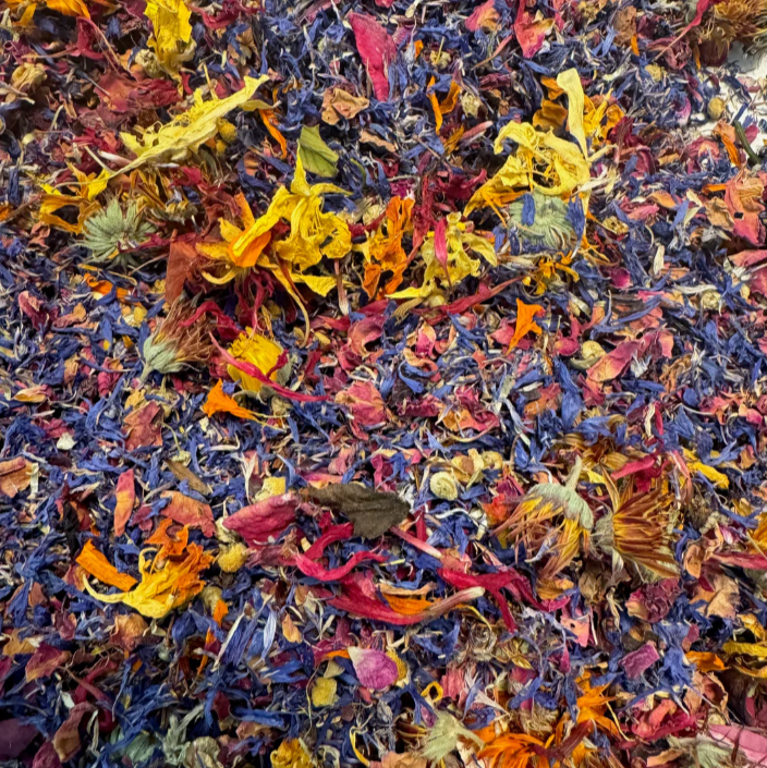 A cream colored tin labeled Edible Flower Mix, with flowers scattered around. 