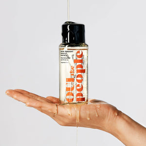 A hand holding a bottle of Oui the People Hydrating Body Gloss 