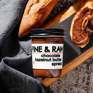 A jar of fine and raw chocolate hazelnut butter spread with a loaf of bread