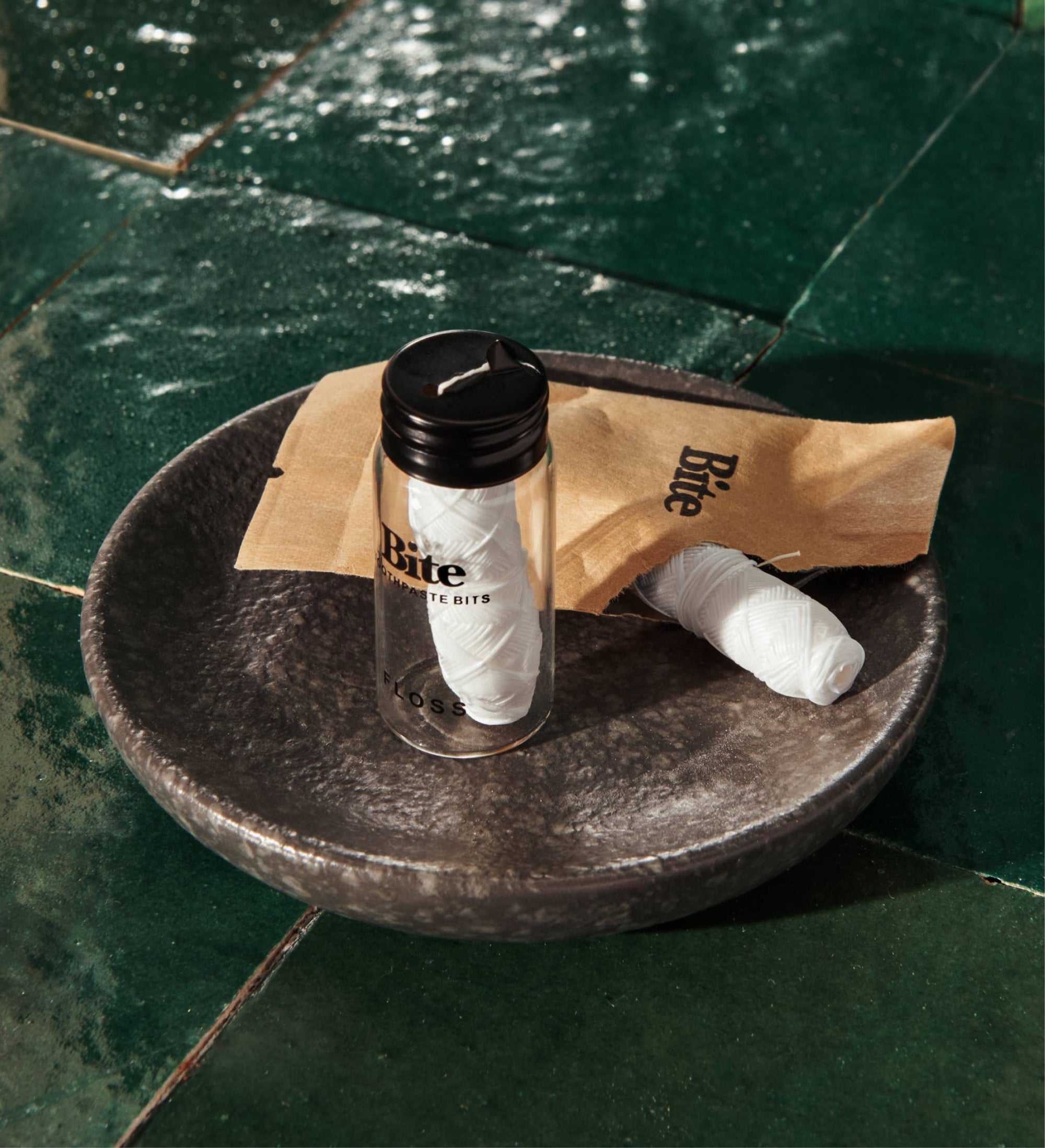 A bottle of Bite floss and a floss refill on a black dish. 