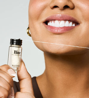 A woman holding a bottle of Bite floss near her mouth. 