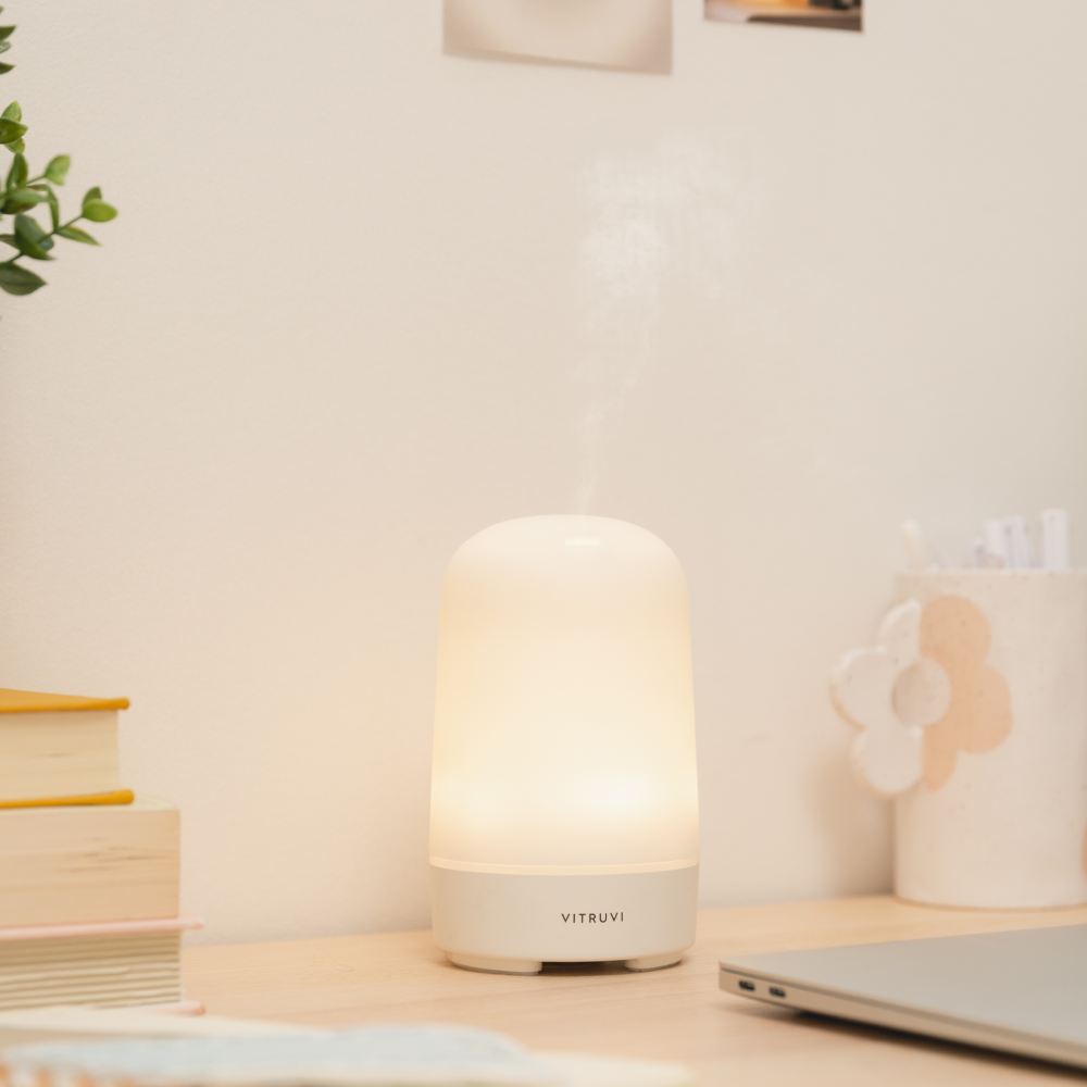 Vitruvi Glow diffuser on a desk with books and a laptop in the background