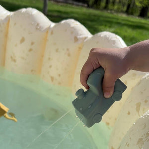 Hand holding a gray toy car over a pool with water splashing
