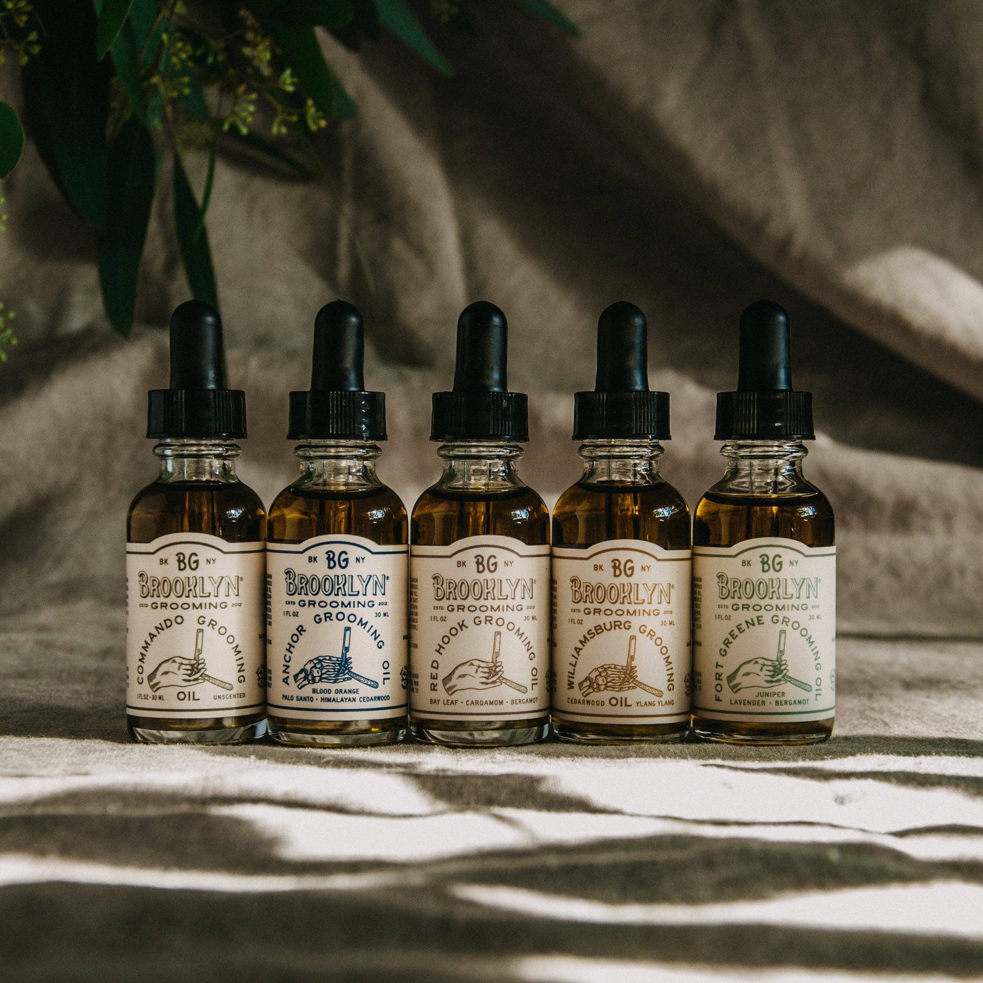 Five Brooklyn Grooming oil products with a fabric background. 