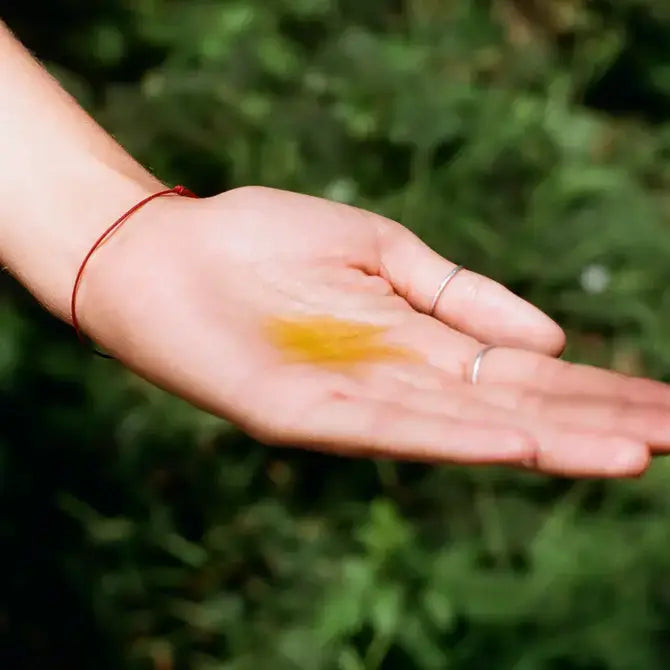 A bottle of Bathing Culture Heat Wave Body Oil with a colorful circular label, placed on a rock outdoors.
