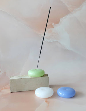Incense stick on a green disc with two other discs below on a soft pink background