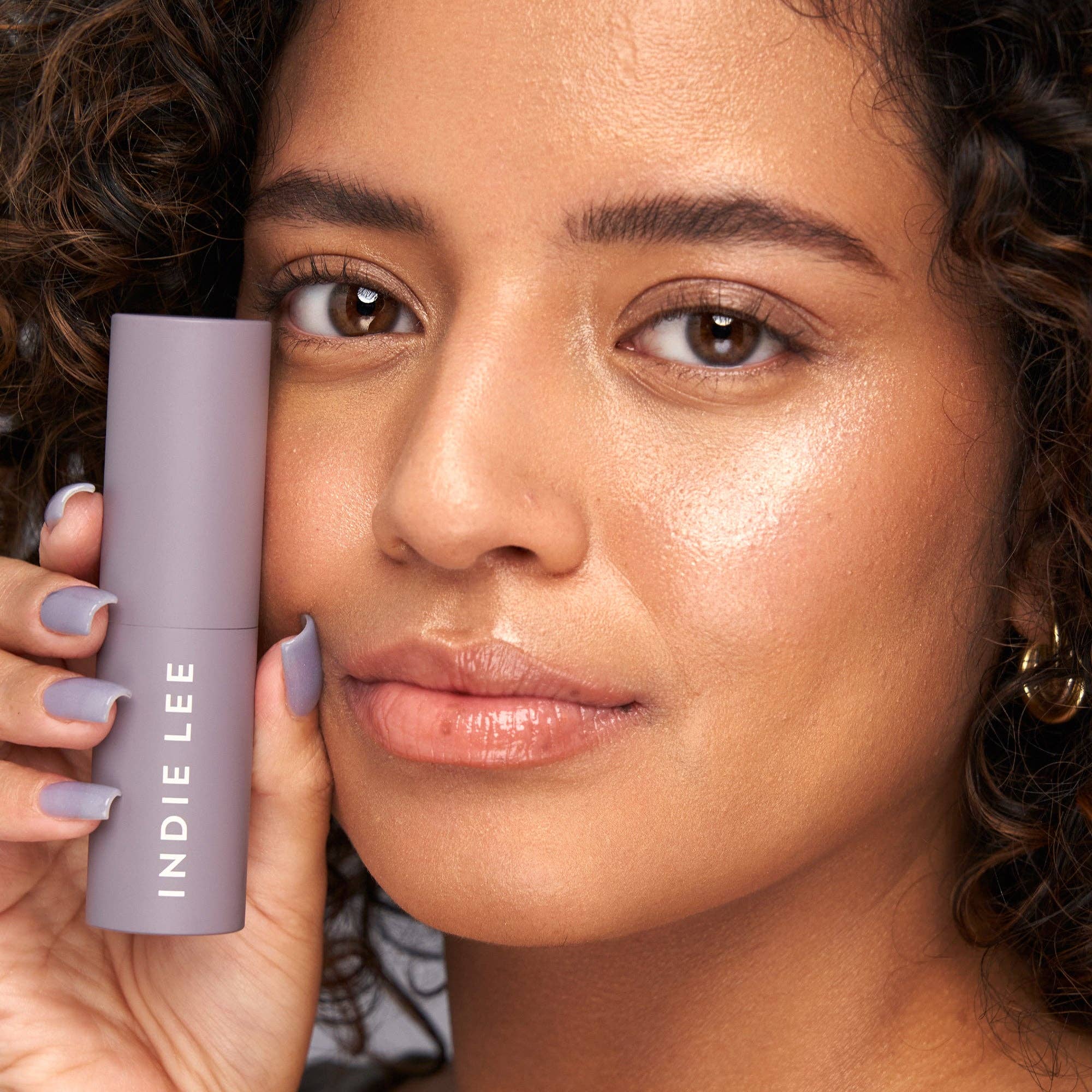Woman holding a purple Indie Lee product close to her face