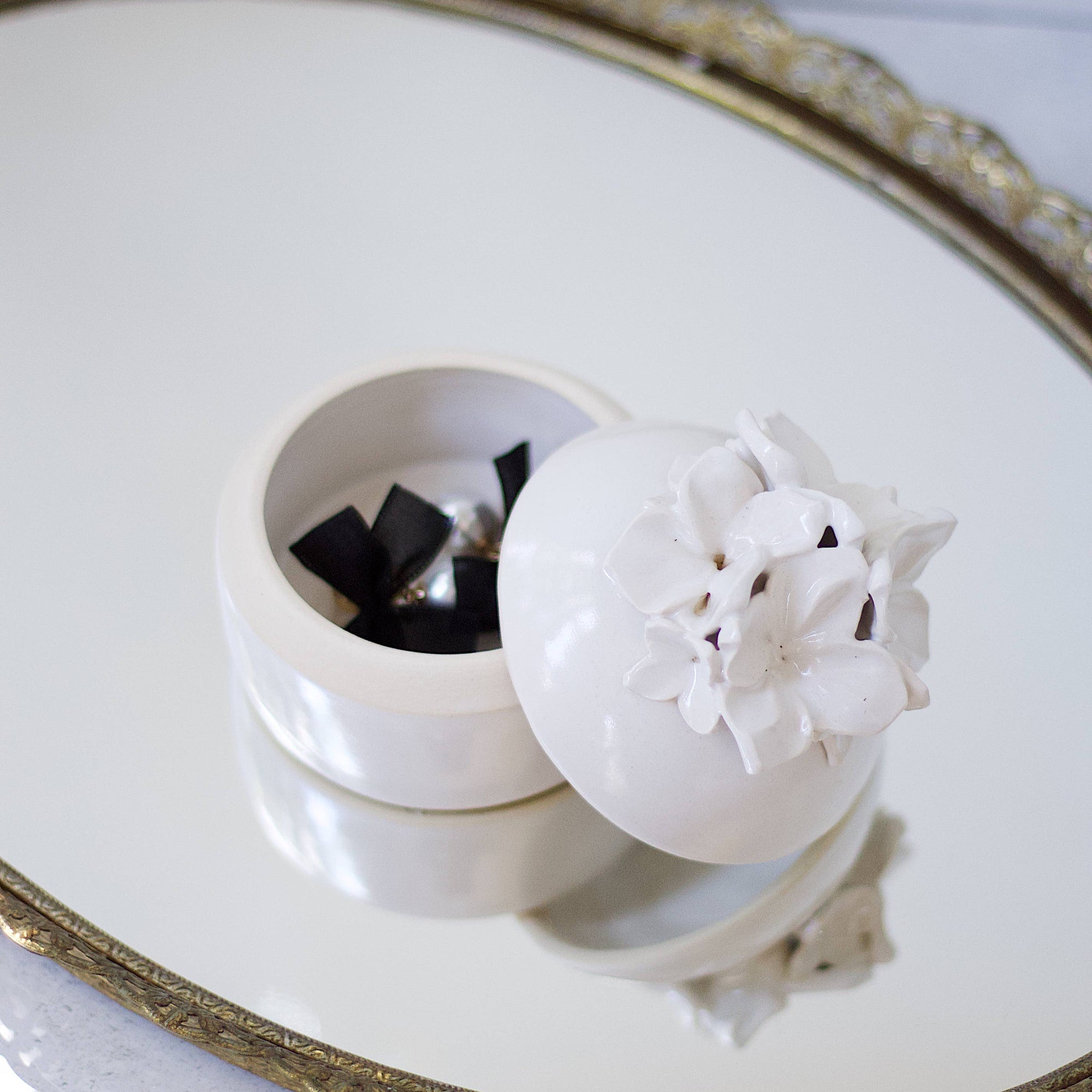 A cream-colored lidded jar with hand-sculpted flowers attached to the lid, placed on a white background.