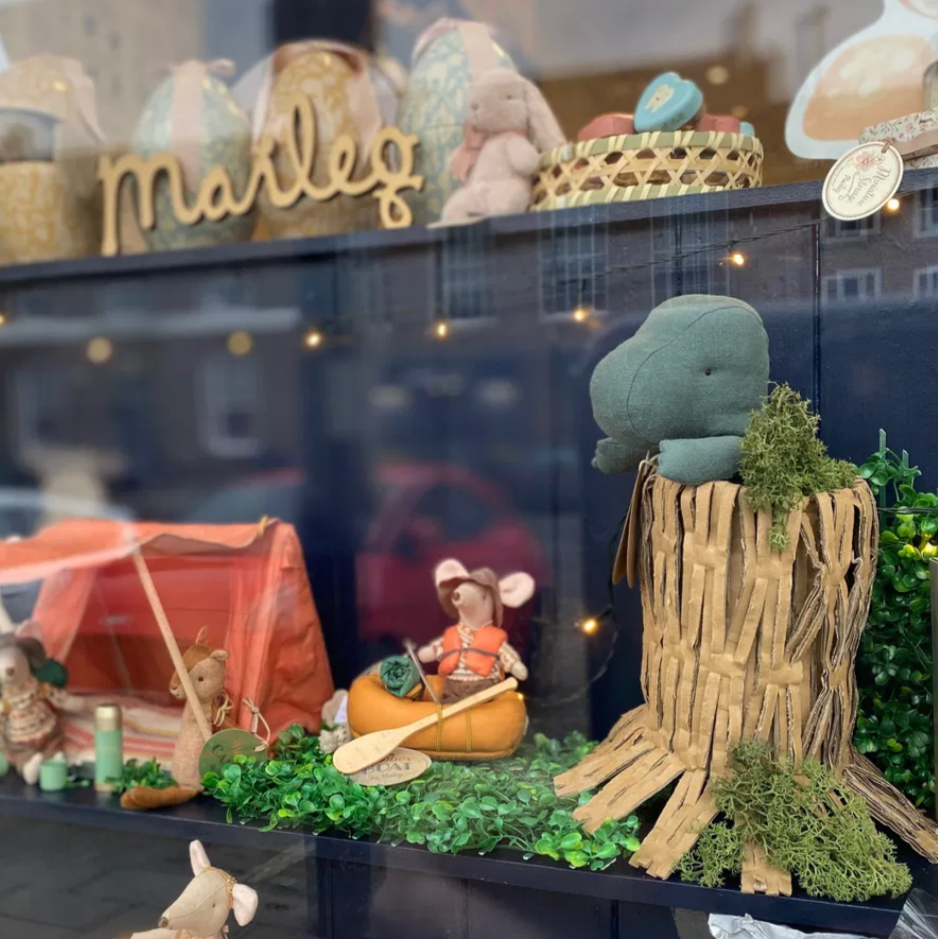 Display of small figurines and decorative items in a window, including a tree stump and camping-themed figures.
