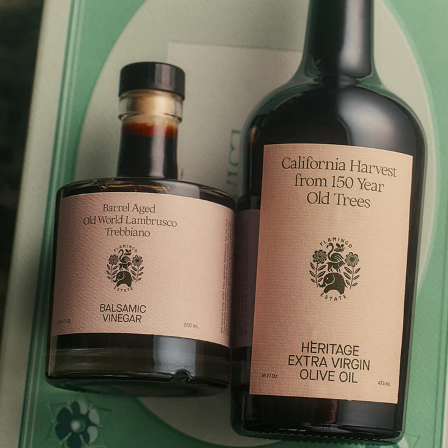 A gift set containing a bottle of olive oil and a smaller bottle of balsamic vinegar, packaged in a box tied with a green ribbon.
