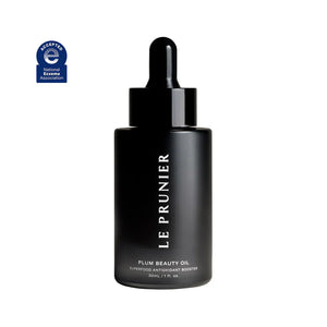 A black bottle with a dropper cap labeled 'Le Prunier Plum Beauty Oil', indicating organic plum seed oil as the main ingredient.
