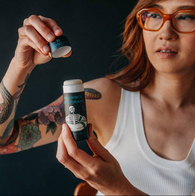 A woman in a white shirt opening a tube of Pilgrim's deodorant. 