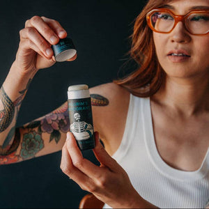 A woman in a white shirt opening a tube of Pilgrim's deodorant. 