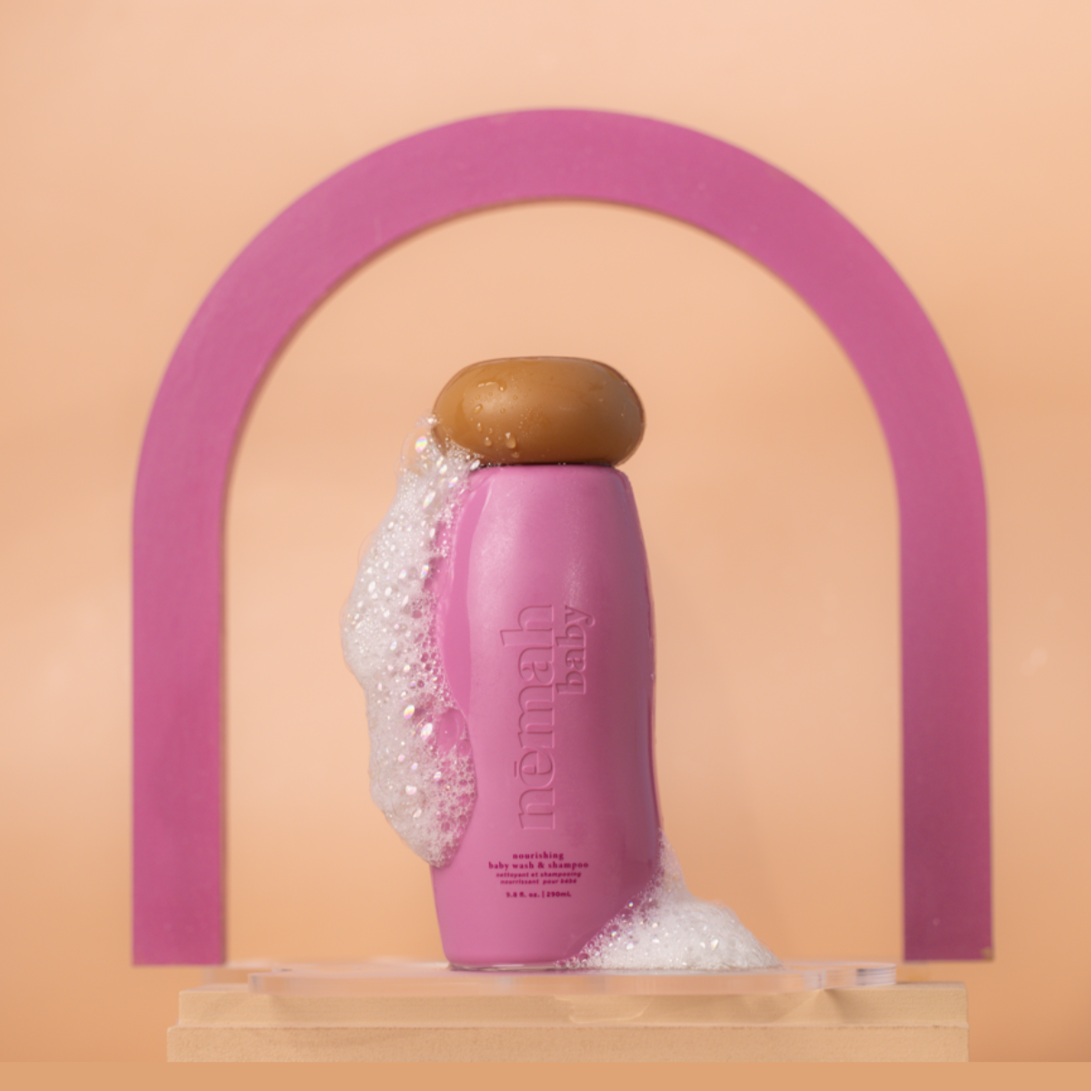 A pink squeeze bottle labeled 'némah' with a brown cap, designed for kids' nourishing wash and shampoo.