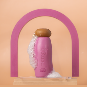A bottle of nomad body wash under a pink rainbow. 