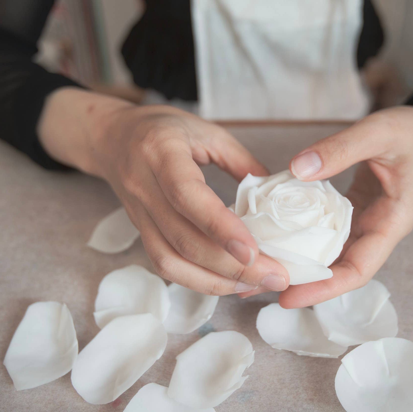 A person assembling a candle shaped like a rose. 