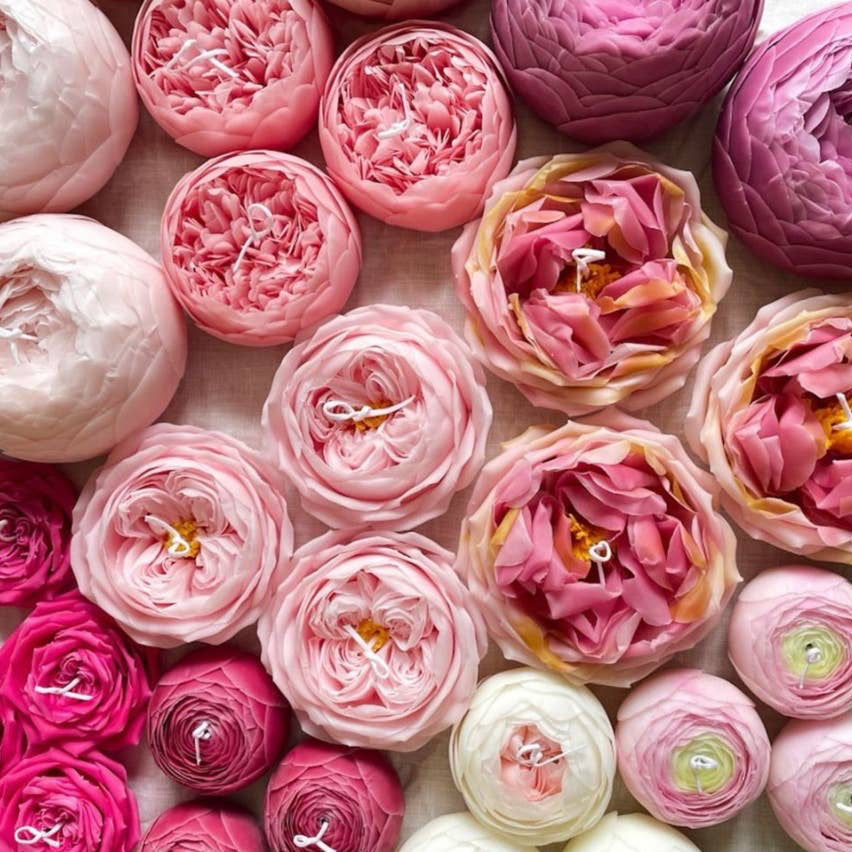 A selection of pink, white, and red candles shaped like roses and peonies. 