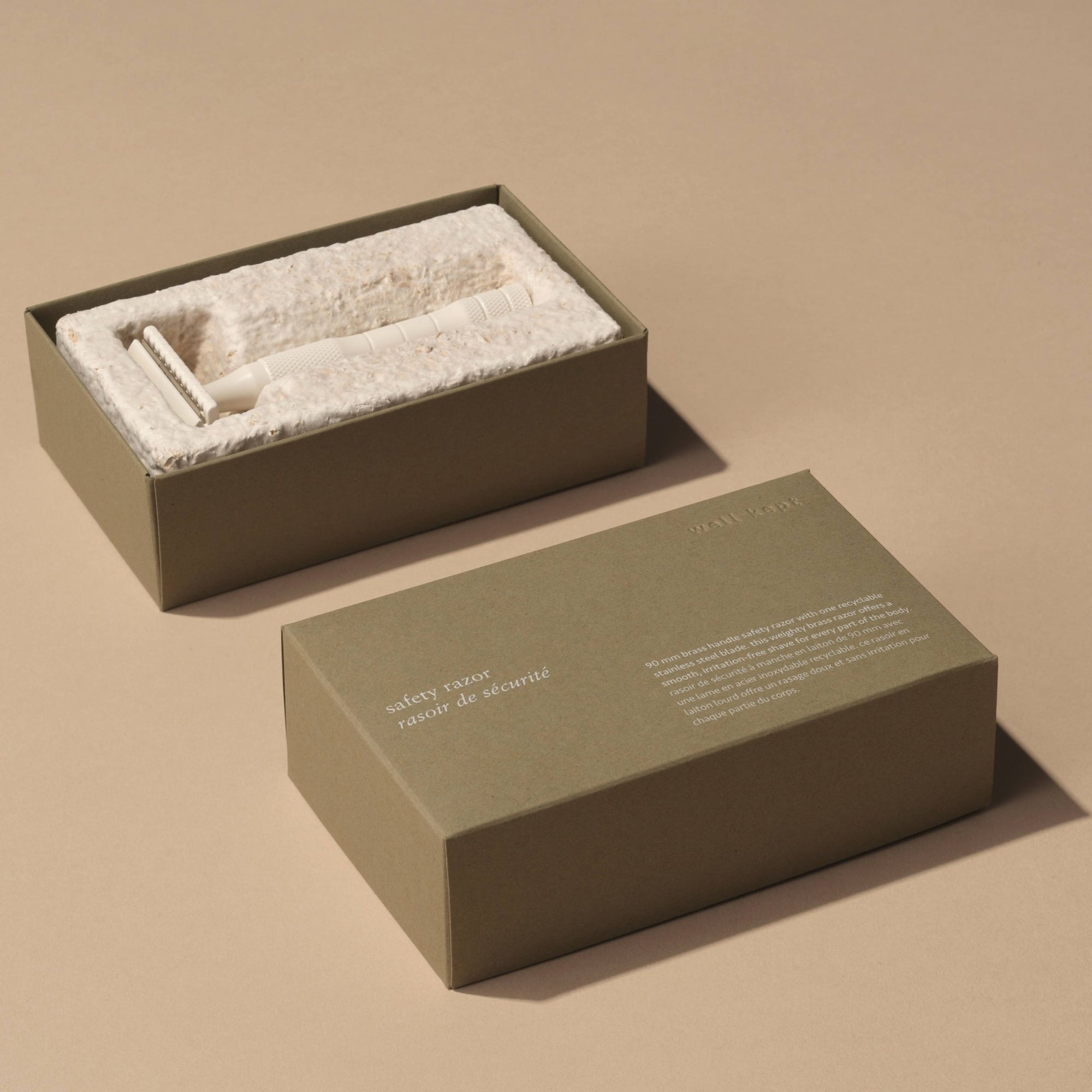A brass safety razor with a stainless steel blade, cream-colored handle, and textured grip area.