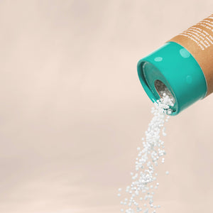 White ocean breeze scent booster pellets pouring out of a brown paper container with a blue top