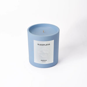 A blue candle with a label reading 'SLEEPLESS AMOLN', indicating the scent and brand.
