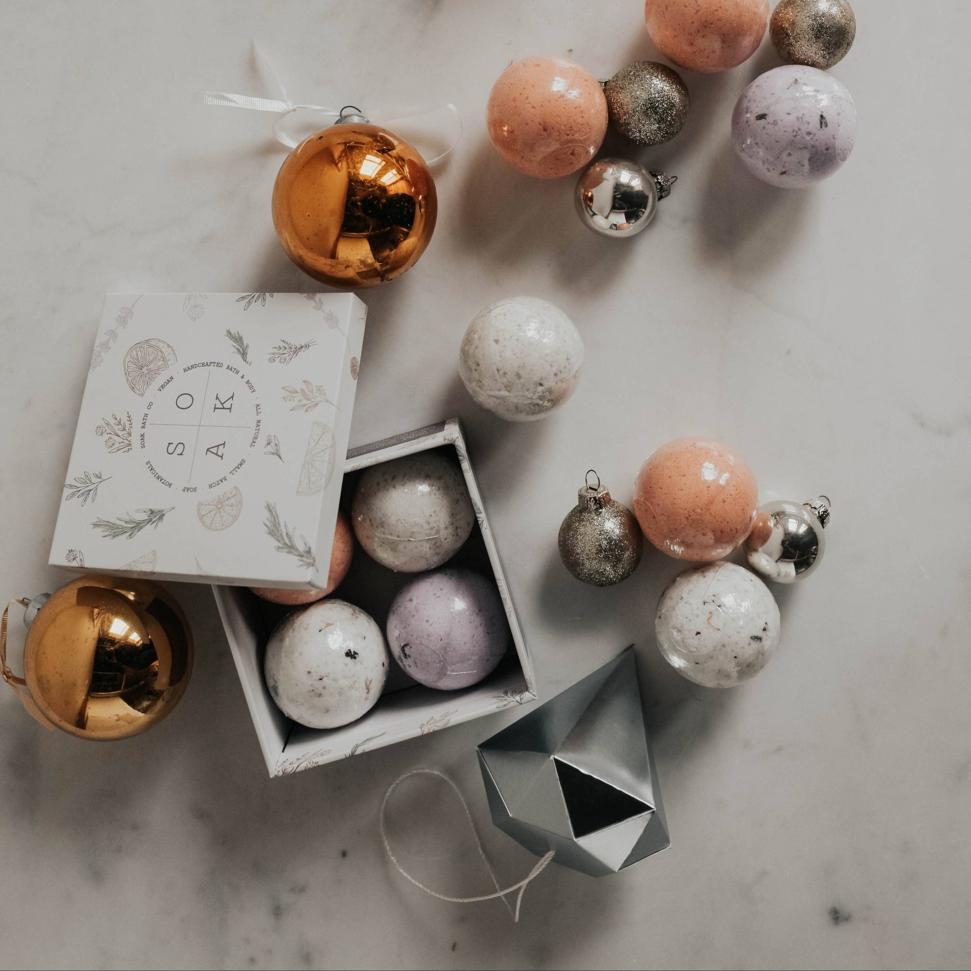 A box of bath bombs surrounded by shiny silver and orange ornaments