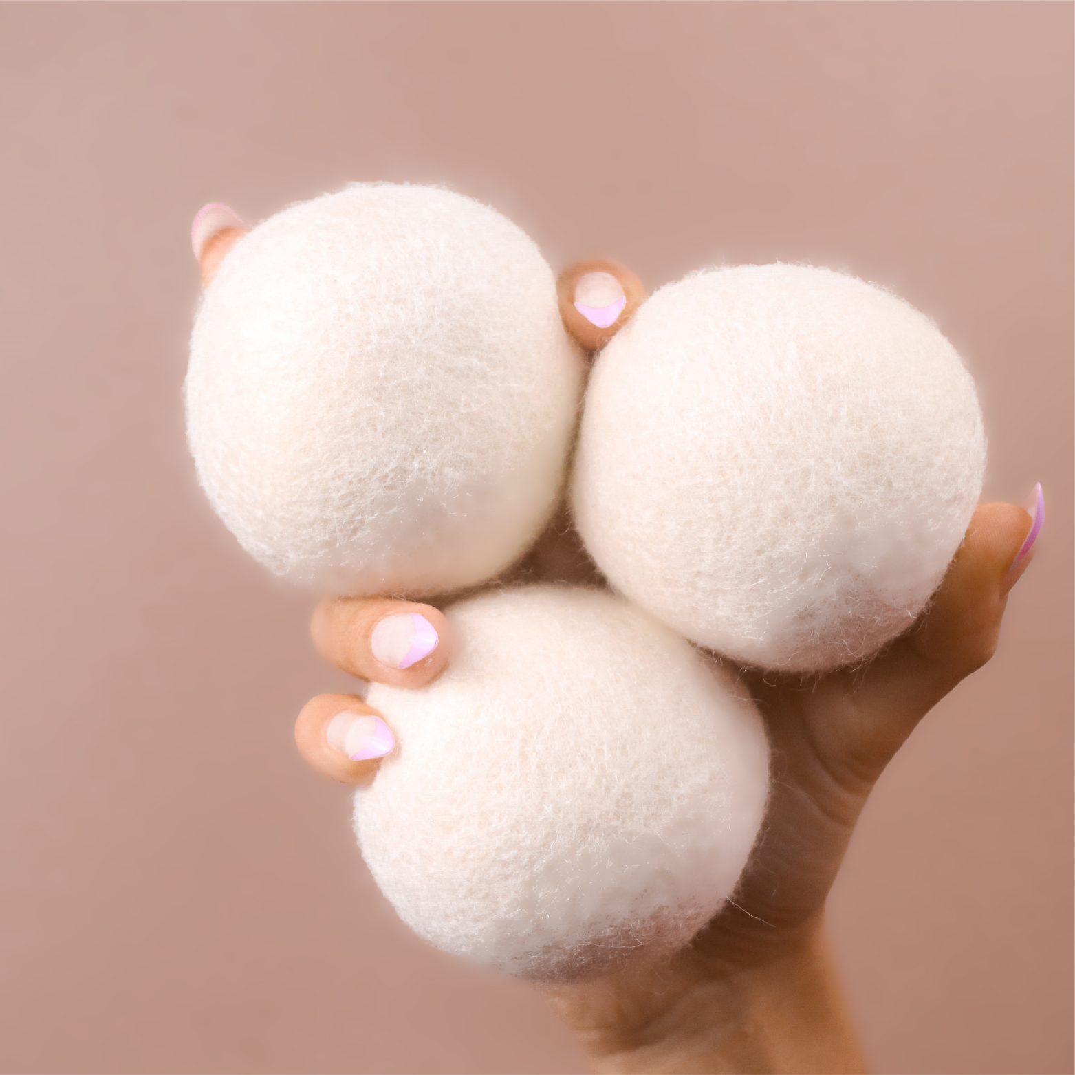Three white wool dryer balls next to a beige package labeled 'Wool Dryer Balls' by Kind Laundry.