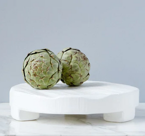 A white trivet holding two artichokes. 
