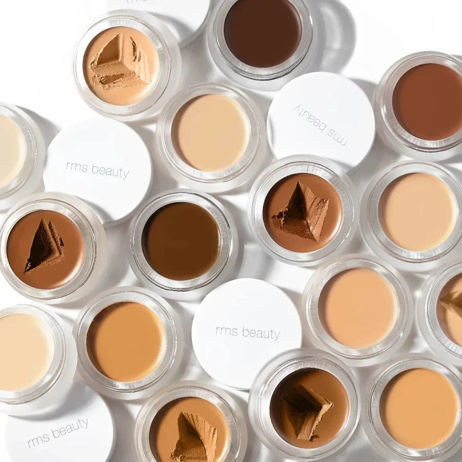 A small glass pan of RMS Beauty UnCoverup Concealer with a white cap that says "RMS Beauty,"