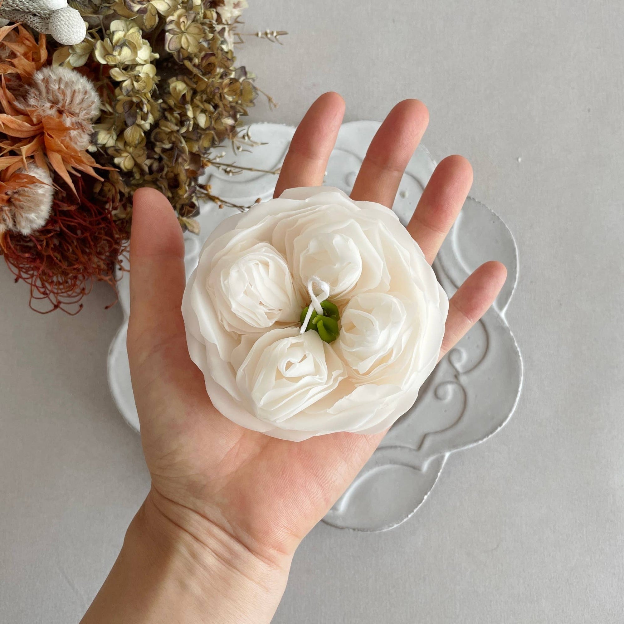 Floral candle on a decorative plate with dried flowers in the background