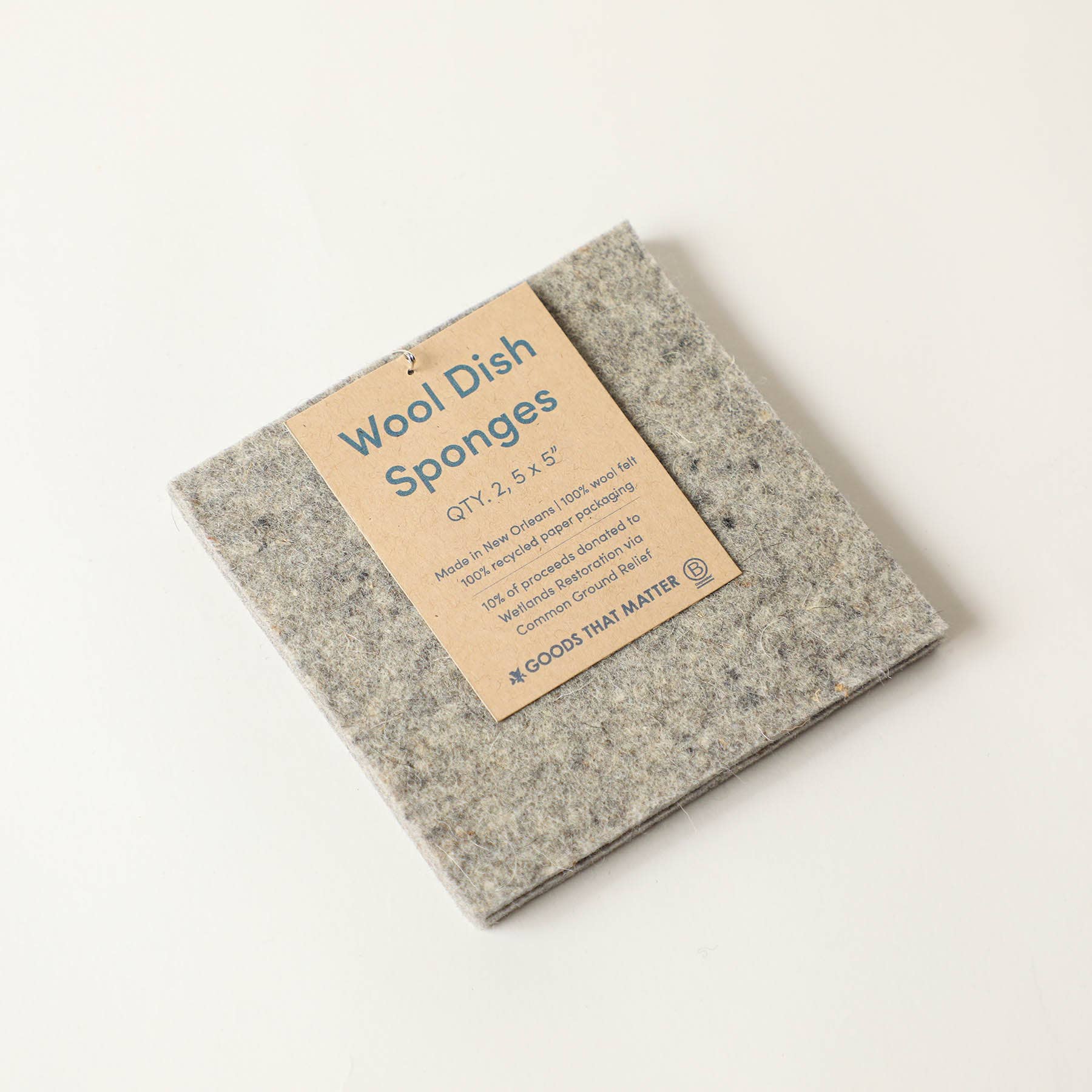 A wool sponge with a brown paper tag, on a light colored surface. 